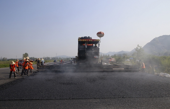 2019年8月，宜春經(jīng)開區(qū)S311路面攤鋪現(xiàn)場，工友們輔助路面兩側(cè)的分料、補(bǔ)窩等作業(yè)